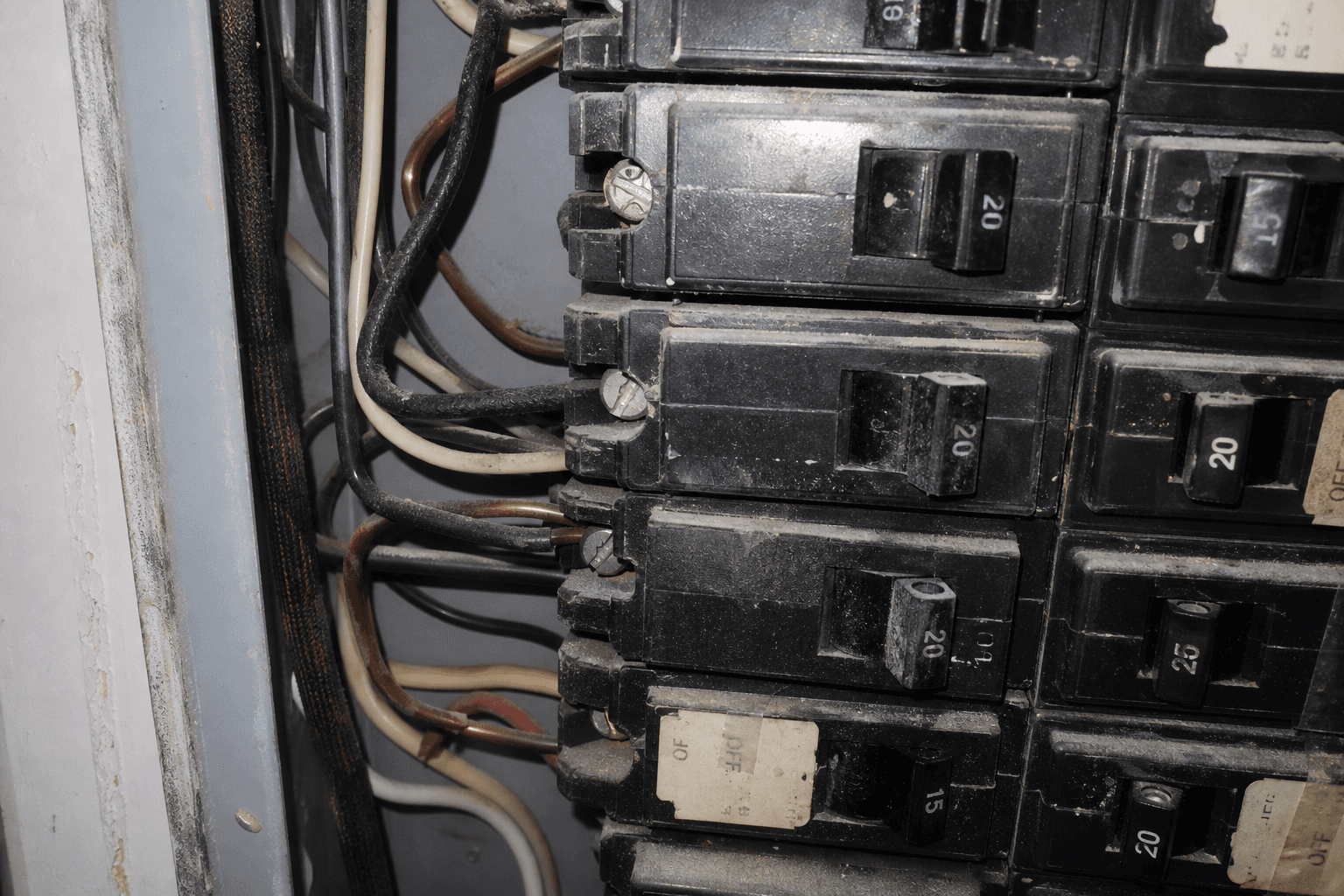 Close-up of an open residential electrical panel with crowded wiring and two conductors under one breaker screw
